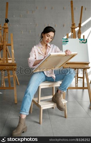 Attractive casual young woman artist holding canvas in hand drawing picture with paints and brush front view. People, leisure and hobby concept. Attractive young woman artist holding canvas in hand drawing picture