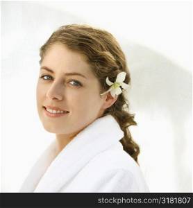 Attractive Caucasian mid-adult woman wearing robe with orchid flower in hair smiling at viewer.