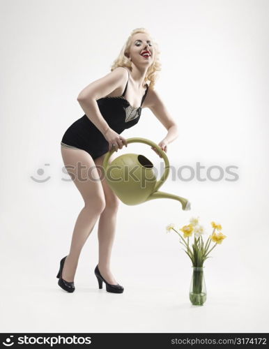 Attractive Caucasian woman wearing retro swimsuit in pinup pose watering daffodils.