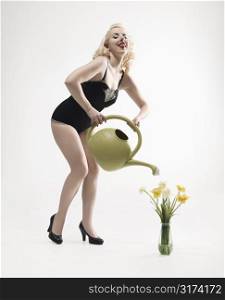 Attractive Caucasian woman wearing retro swimsuit in pinup pose watering daffodils.