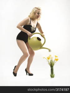 Attractive Caucasian woman wearing retro swimsuit in pinup pose watering flowers.