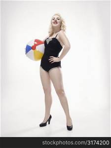 Attractive Caucasian woman wearing retro swimsuit in pinup pose with beach ball.