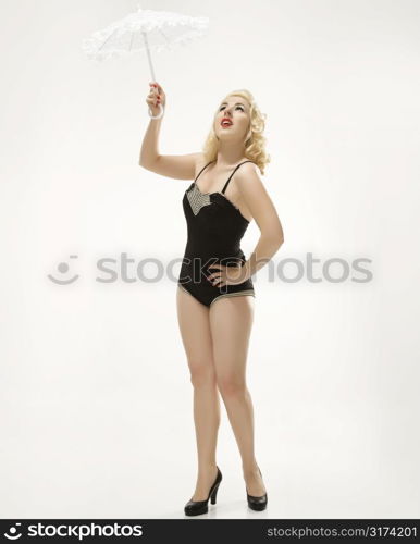 Attractive Caucasian woman wearing retro swimsuit in pinup pose with umbrella.