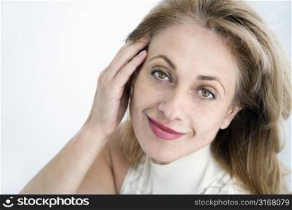 Attractive Caucasian woman with hand to face smiling at viewer.