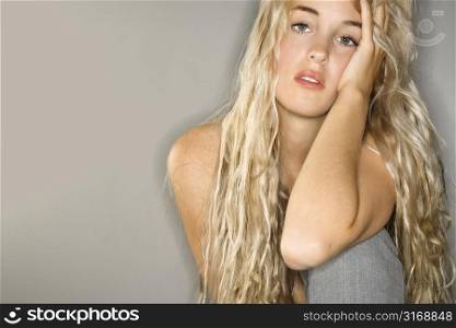 Attractive Caucasian woman with long blonde hair looking at viewer with head resting on hand.