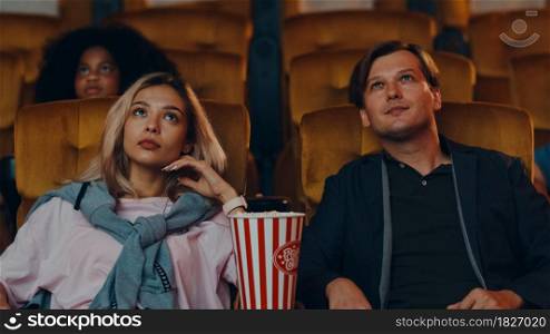 Attractive cheerful young caucasian couple laughing while watching film in movie theater. Lifestyle entertainment concept.