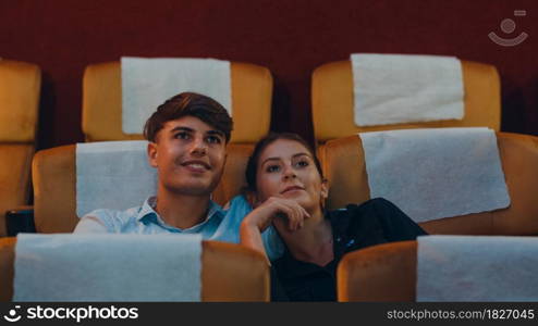 Attractive cheerful young caucasian couple laughing while watching film in movie theater. Lifestyle entertainment concept.