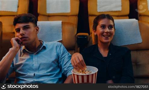Attractive cheerful young caucasian couple laughing while watching film in movie theater. Lifestyle entertainment concept.