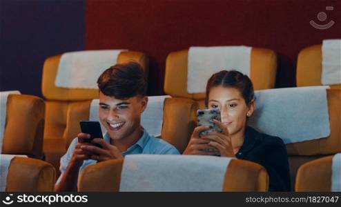 Attractive cheerful young caucasian couple using smartphone while watching film in movie theater. Lifestyle entertainment concept.