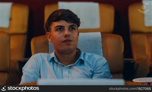 Attractive cheerful young caucasian man laughing while watching film in movie theater. Lifestyle entertainment concept. Close up shot.