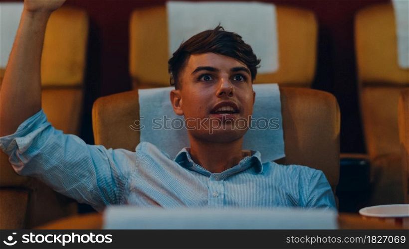 Attractive cheerful young caucasian man laughing while watching film in movie theater. Lifestyle entertainment concept. Close up shot.