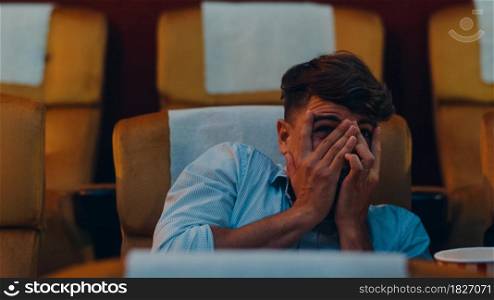Attractive cheerful young caucasian man watching horror movie in cinema theater. Lifestyle entertainment concept. Close up shot.