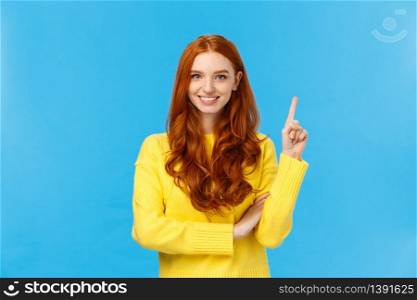 Attractive confident and charismatic caucasian redhead female in yellow sweater, showing number one, order product, being first, smiling satisfied and assertive, standing blue background.. Attractive confident and charismatic caucasian redhead female in yellow sweater, showing number one, order product, being first, smiling satisfied and assertive, standing blue background