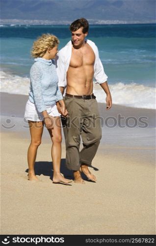Attractive couple holding hands walking on beach smiling at eachother in Maui, Hawaii.