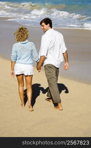 Attractive couple holding hands walking on beach smiling at eachother in Maui, Hawaii.