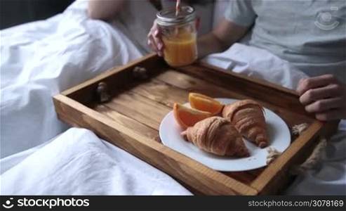 Attractive couple in love spending leisure together in bedroom while communicating and having romantic breakfast in bed at home. Joyful young family talking and drinking orange juice while sharing breakfast in morning. Slow motion. Steadicam shot.