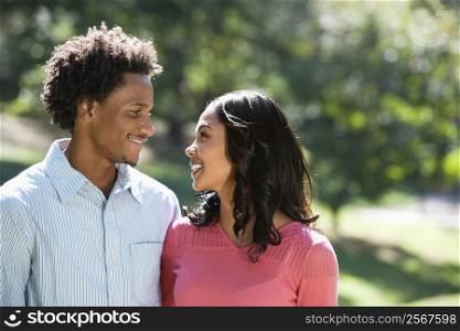 Attractive couple in park looking at eachother smiling.