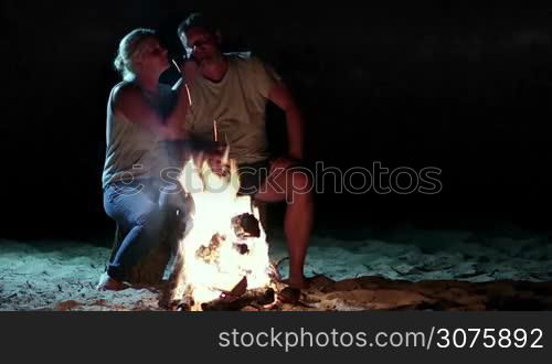 Attractive couple resting near bonfire at night. Couple relaxing near campfire. They gently hugging and kissing