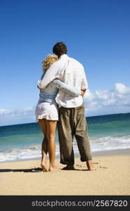 Attractive couple standing embracing looking out at ocean in Maui, Hawaii.