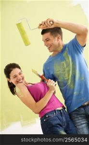 Attractive couple standing in front of partially painted wall playfully putting paint on eachother.