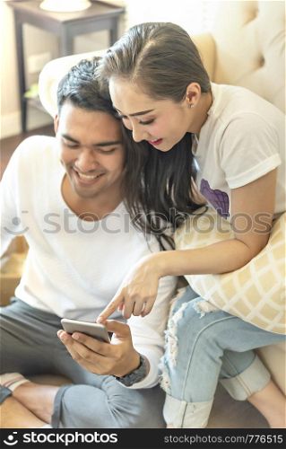 attractive couple using smartphone together on sofa at home. couple using smartphone together