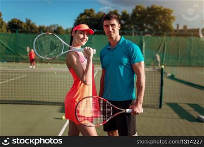 Attractive couple with tennis rackets together on outdoor court. Summer season active sport game