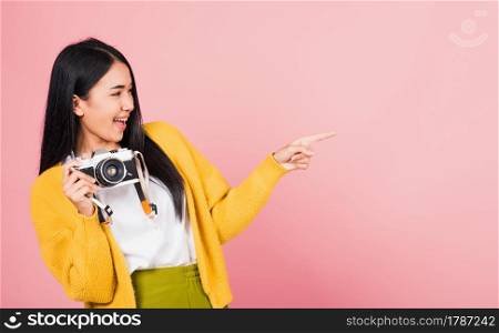 Attractive energetic happy Asian portrait beautiful cute young woman teen excited smiling holding vintage photo camera and pointing finger to side space, studio shot isolated on pink background
