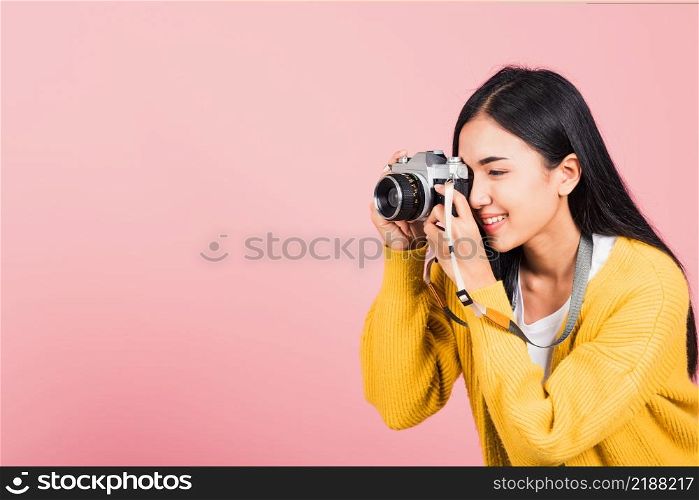 Attractive energetic happy Asian portrait beautiful young woman smiling photographer taking a picture and looking viewfinder on retro vintage photo camera ready to shoot isolated on pink background