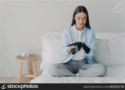 Attractive european girl adjusting her cyber arm in morning at home. Artificial hand and arm with wrist joint. Disabled young woman assembling prosthesis. Bionic hand has processor chip and sensors.. Attractive european girl adjusting her cyber arm at home. Artificial hand and arm with wrist joint.