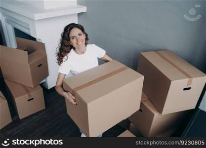 Attractive european girl in white t-shirt is leaving house. Lady is packing cardboard boxes and carrying. Cheerful young woman is going to buy apartment. Relocation and independence concept.. Attractive european girl in white t-shirt leaving house. Lady packing and carrying cardboard boxes.