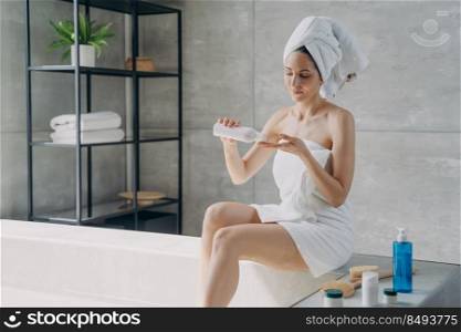Attractive european woman wrapped in towel applying body lotion after bathing. Young woman takes shower in morning at home. Anti-cellulite massage and bodycare. Daily beauty routine and spa procedure.. Attractive european woman wrapped in towel applying body lotion after bathing. Daily beauty routine.