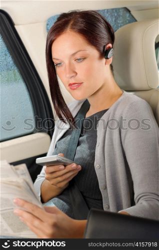 Attractive executive businesswoman sitting in car calling phone checking newspapers