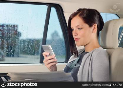 Attractive executive businesswoman sitting in car looking phone holding newspapers