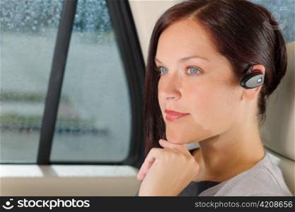 Attractive executive female manager sitting in car backseat calling hands-free
