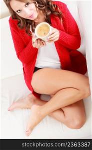 Attractive fall girl red autumnal sweater holding white mug with coffee warm beverage, sitting on sofa at home. Woman warming herself relaxing top view