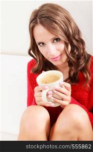 Attractive fall girl red autumnal sweater holding white mug with coffee warm beverage, sitting on sofa at home. Woman warming herself relaxing top view