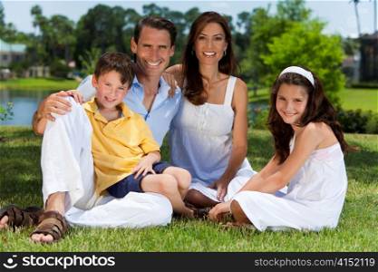 Attractive Family Sitting On Grass Outside In Sunshine