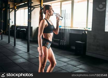 Attractive female athlete drink water after training in gym. Slim woman in fitness club