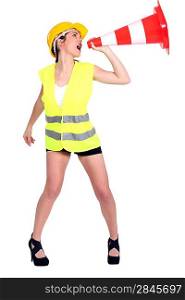 Attractive female construction worker shouting into traffic cone