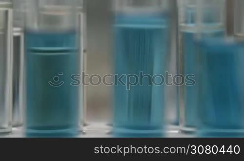 Attractive female scientist in eyeglasses with pipette dropping samples into test tubes in chemical laboratory. Selective focus. Pipette adding chemical fluid into several test tubes with liquid. Researcher dropping the reagent into test tubes in lab