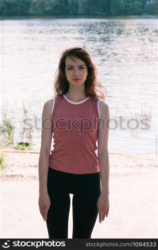 Attractive fit female practicing sports activity, yoga, wearing tight clothes, stretching pose, hands along the body, long hair, water background. Healthy lifestyle, keep fit, weight loss concept