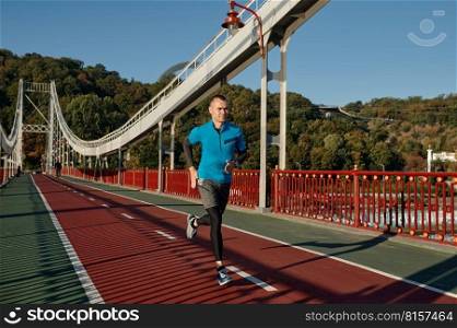 Attractive fit man running fast along the bridge. Jogger doing outdoors workout in morning. Attractive fit man running fast along the bridge