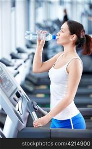 Attractive girl drinking water on a treadmill