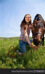 attractive girl feeding a horse apples. outdoor shot