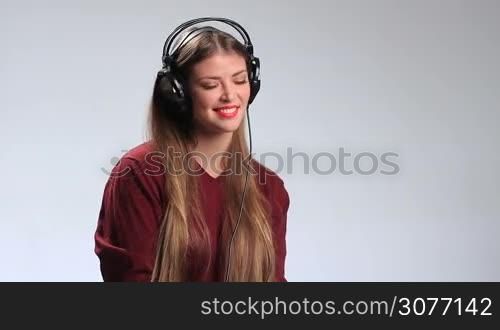 Attractive girl listening to the misic in massive stylish headphones. Seductive brunette woman with red lipstick enjoying favorite song on the radio, twisting her beautiful long hair around her finger, looking at camera temptingly and alluringly.