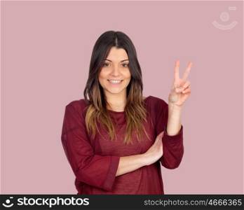 Attractive girl making the victory symbol on a pink background