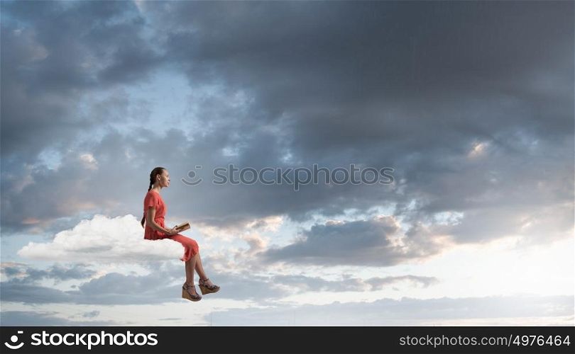Attractive girl read book. Young woman in dress with old book in hand sitting on cloud
