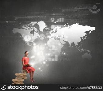 Attractive girl reading book. Young girl in red dress sitting on stack of books and reading