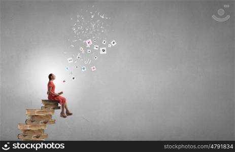 Attractive girl reading book. Young girl in red dress sitting on stack of books and reading