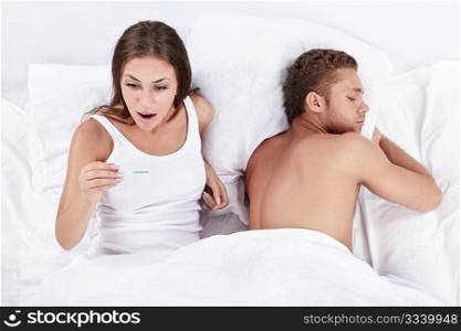 Attractive girl stares at a test for pregnancy in bed